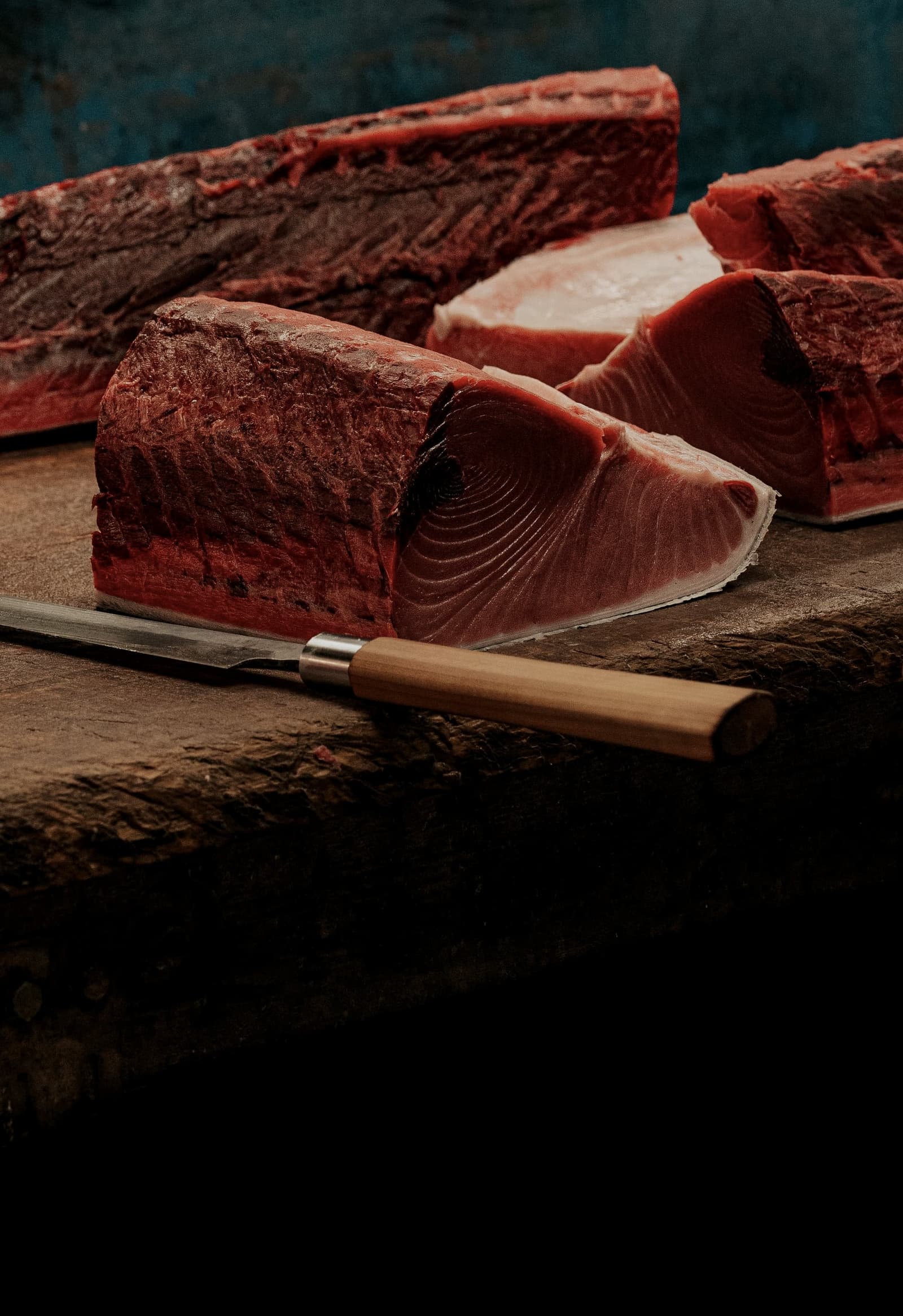 Blocks of bluefin on a wooden board with a long knife