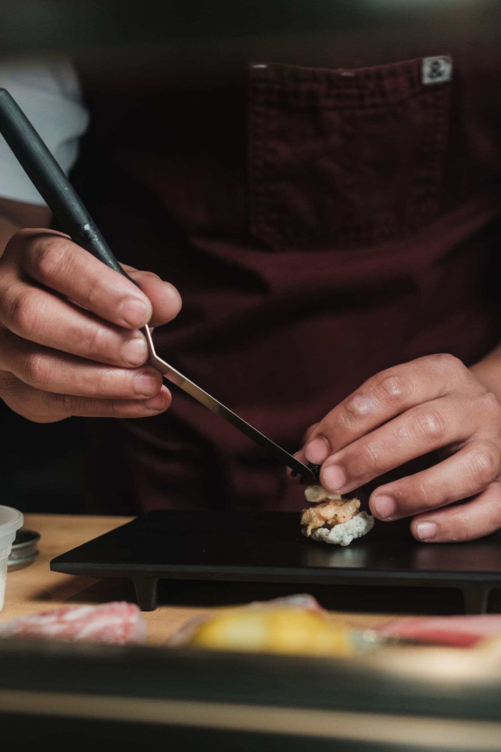 A chef's hands placing a piece of nigiri with fine tweezers