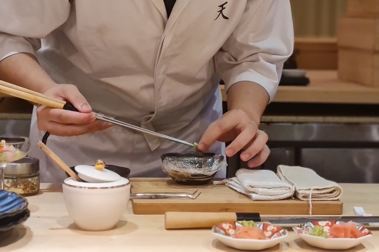 A chef leaning in over the counter, placing a garnish with chopsticks