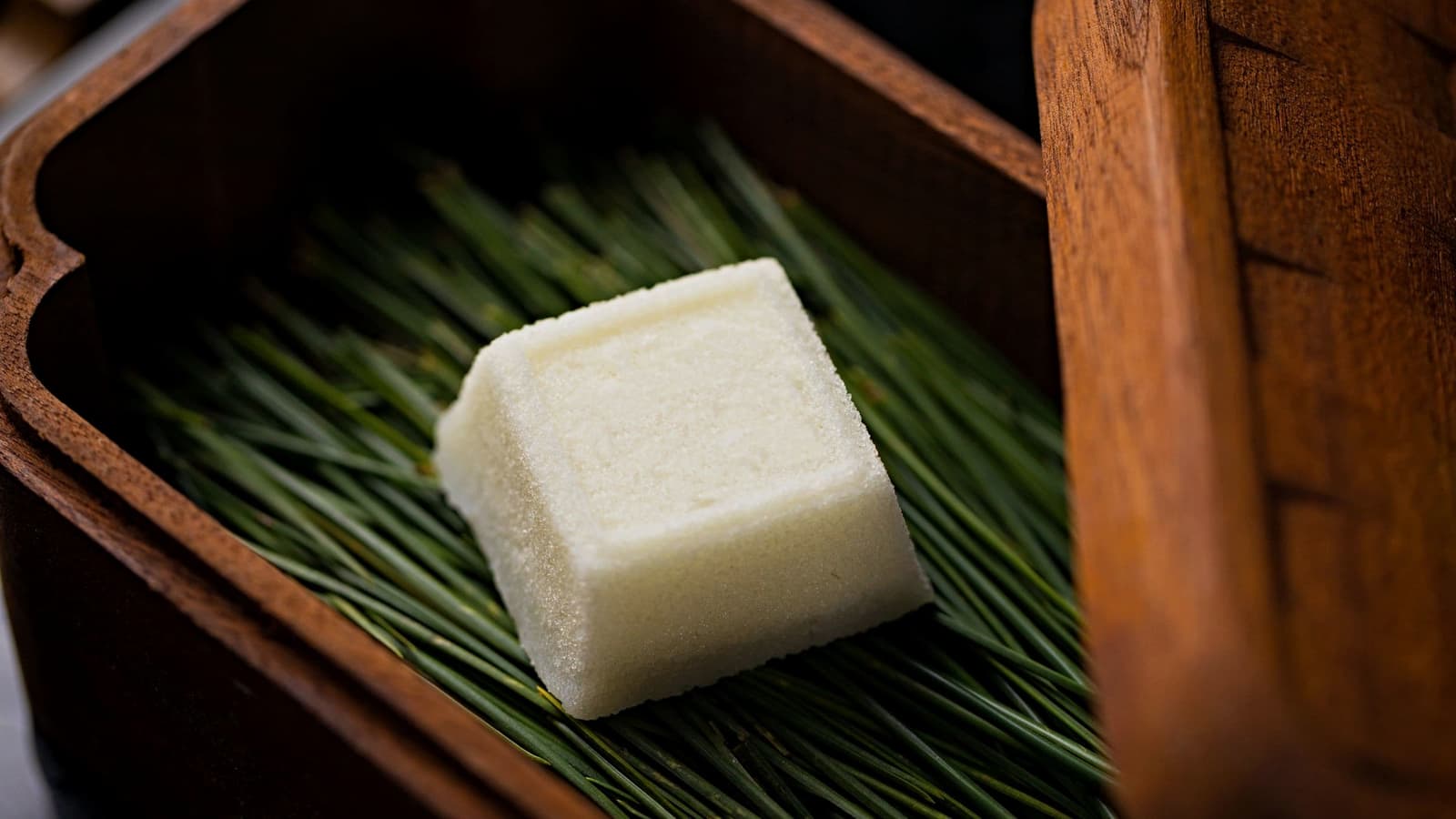 A pale square of milk kanten on a bed of green, in a wooden tray