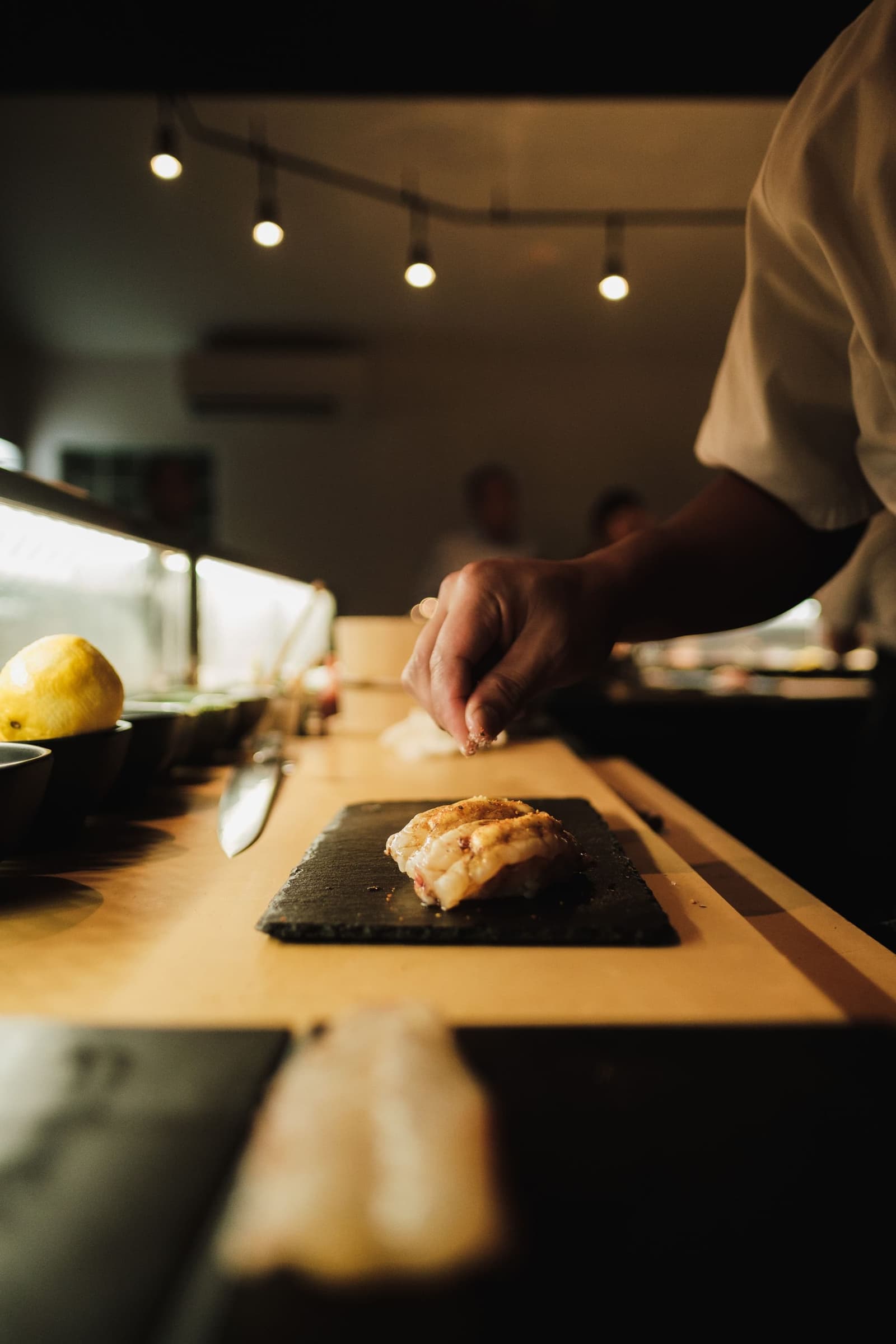 A chef setting a piece of nigiri on a slate at the counter