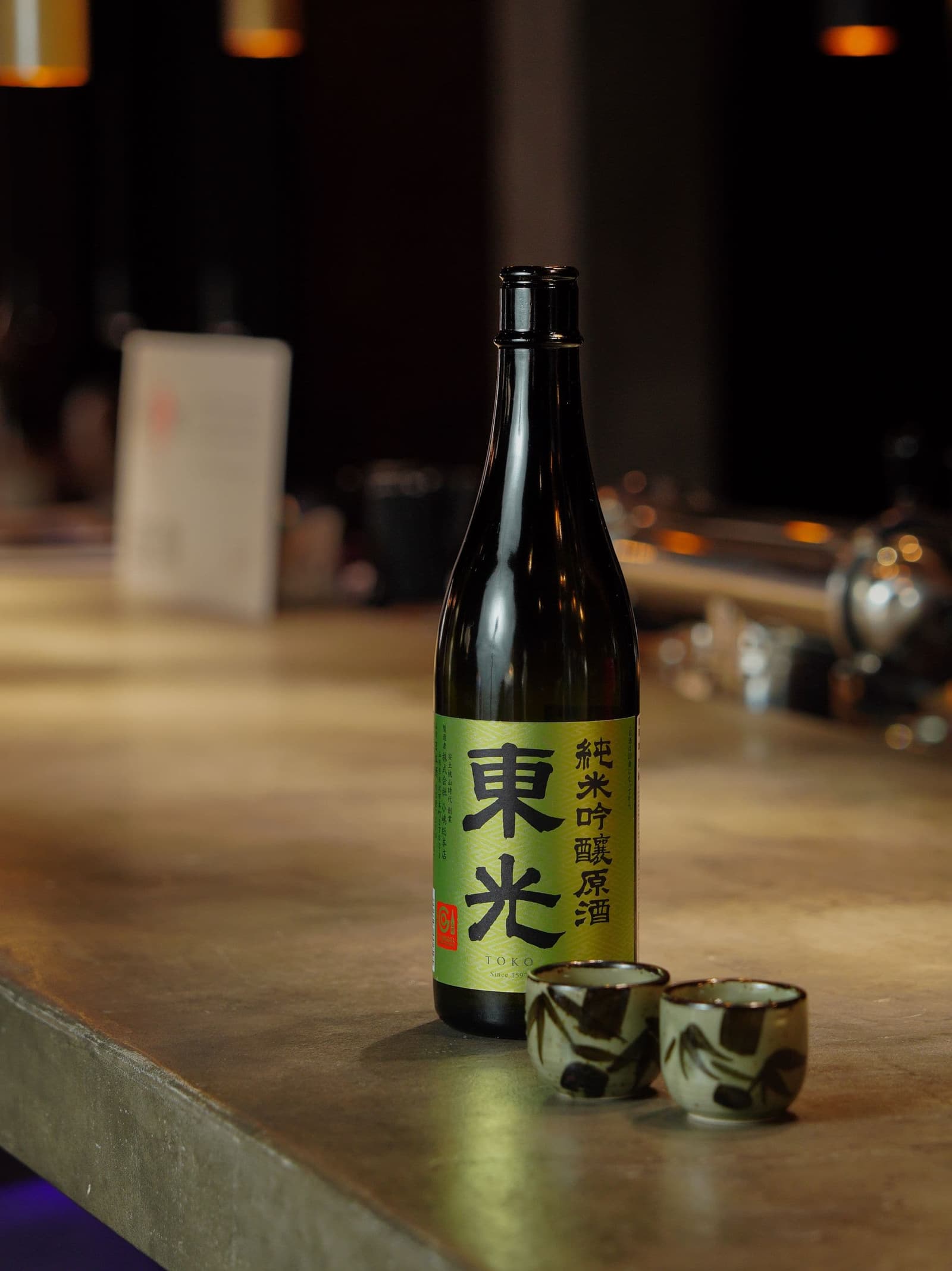A bottle of junmai ginjo sake and two small cups on a stone bar
